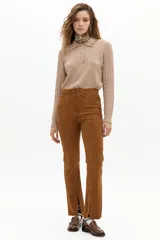 Pantalón de corte recto confeccionado en gamuza de cabra color marrón tostado. Presenta tiro medio con elástico interno en la cintura, cierre frontal con gancho metálico y tajos en el ruedo.