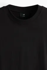 Remera negra de punto de algodón de peso medio, cuello redondo ribeteado y hombros caídos con corte relajado.