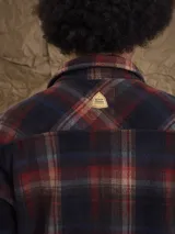 Sobrecamisa de tejido polar con estampado abstracto en tonos rojizos y azul marino. Presenta cuello clásico, cierre frontal con botones a presión, dos bolsillos frontales con solapa en el pecho y un parche decorativo.