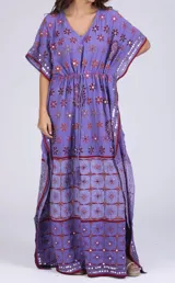 Vestido largo lila con estampado de flores rojas y espejos. Tiene escote en V, mangas cortas y cintura ajustable con cordón.