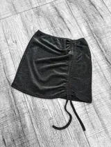 Minifalda negra con lurex, corte ajustado y detalle de frunce lateral con cordones.