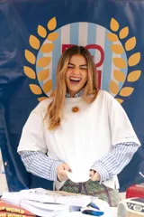 Remera blanca de algodón de corte oversize, con cuello redondo y bordado de sol en el centro del pecho. Se presenta combinada con una camisa de rayas verticales debajo.