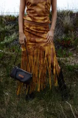 Pollera midi de cuero con estampado marmolado en tonos marrones y mostaza, de corte asimétrico con detalles de largos flecos colgantes en el borde inferior.