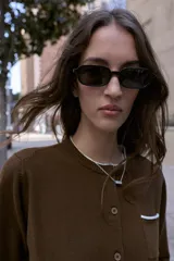 Chaqueta de punto color marrón con cuello redondo, manga larga y cierre frontal con botones. Presenta un bolsillo delantero tipo plastrón y detalles de ribetes en color celeste en el cuello y el bolsillo.