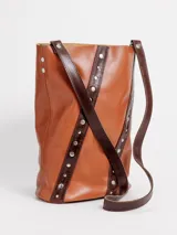 Matera bucket de cuero rojo con detalles en cuero negro y tachas metálicas plateadas dispuestas en líneas diagonales. Cuenta con una manija superior corta.