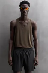 Pantalón corto deportivo color marrón oliva, confeccionado en tejido técnico ligero y elástico, con forro interior. Presenta cintura elástica ajustable con cordón, bolsillos frontales, bolsillo de seguridad trasero con cierre y aberturas laterales en el bajo.