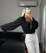 Blusa de tela cey color bordó, con escote en V y mangas largas abullonadas que terminan en puños con detalle de encaje y volados.