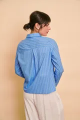 Camisa de manga larga color celeste con rayas verticales blancas, cuello camisero y volados frontales a lo largo de la botonera.