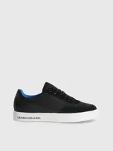 Zapatillas urbanas Calvin Klein con diseño de corte bajo. Presentan una combinación de materiales en la capellada, incluyendo paneles de nailon, cuero y ante en color negro. Destacan por su suela de goma blanca con el logo de la marca estampado en el lateral, forro interior en color azul vibrante y cierre mediante cordones.
