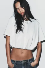 Camiseta cropped blanca de algodón 100%, con cuello redondo, manga corta y bajo abullonado con pliegues.