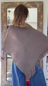 Poncho tejido en lana merino color marrón, con diseño de punto acanalado y terminación con flecos en el borde inferior. Incluye una pequeña etiqueta de cuero en la parte posterior.