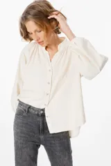 Camisa de pana color verde oliva, con cuello mao, cierre frontal de botones y mangas largas abullonadas con puños elásticos.