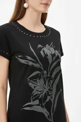 Remera negra de manga corta, con cuello redondo y ajuste al cuerpo. Cuenta con un gran estampado floral en tono gris en el frente y detalle de tachas plateadas alrededor del cuello y en los puños.