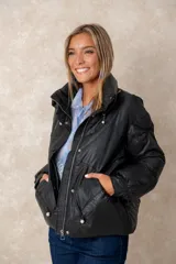 Campera puffer de acabado satinado en color beige, con cuello alto, cierre frontal y bolsillos laterales. Presenta un diseño moderno y sofisticado.