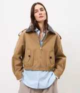 Campera Comfort de poliéster color camel, con cuello de poliuretano en contraste color marrón oscuro, cierre frontal y bolsillos con solapa y botones. Presenta martingalas en los hombros y elástico en la cintura.