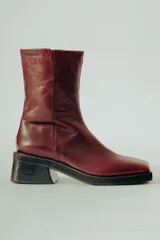 Bota de caña media confeccionada en cuero natural color bordó, con diseño minimalista, punta cuadrada y taco ancho de altura media.