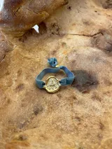 Pulsera dorada con dije redondo con la imagen de la Virgen de Fátima y cinta de terciopelo elástico color verde petróleo.