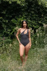 Traje de baño enterizo negro con lunares blancos, de un solo hombro y con abertura en el pecho.