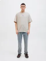 Remera beige de manga corta y cuello redondo con estampado en la espalda con la inscripción "Atelier © 1990" y un diseño abstracto en tonos lila y naranja.