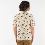 Camisa de manga corta color beige con estampado tropical de palmeras y veleros, cuello abierto y bolsillo en el pecho.