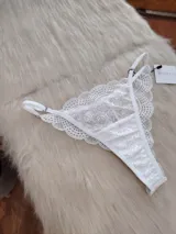 Tanga tipo colaless confeccionada en encaje blanco con diseño floral, cuenta con tiras laterales regulables y refuerzo de algodón en la entrepierna.