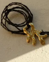 Collar con dije de bronce macizo con forma orgánica irregular, similar a un coral, suspendido de un cordón negro de seda natural anudado.