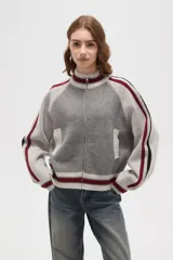 Campera de punto con cierre frontal, cuello alto y diseño de rayas laterales en mangas. Presenta un patrón texturizado en el cuerpo y detalles de rib acanalado en puños, cuello y ruedo.