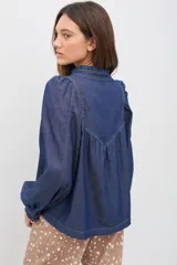 Camisa de denim azul con costuras a la vista en color contrastante, cuello camisero, mangas largas abullonadas con puños abotonados y corte holgado.