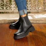 Bota tipo Chelsea de cuero vacuno, con suela de goma track de doble altura y elásticos laterales. Presenta una horma de punta cuadrada.