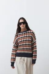 Sweater de punto con diseño geométrico de rombos en tonos azul, marrón, beige y blanco. Presenta cuello redondo, puños y ruedo acanalados en color azul oscuro, con un calce relajado y mangas largas.