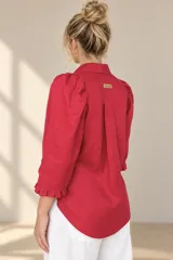 Camisa de lino color blanca, con cuello clásico, mangas tres cuartos abullonadas en los hombros y terminación con volados en los puños, cierre frontal con botones ocultos.