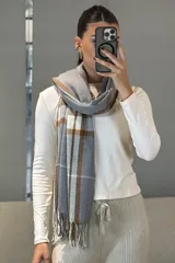 Bufanda rectangular de tejido suave con diseño de cuadros escoceses en tonos mostaza, blanco y gris, terminada con flecos en los extremos.