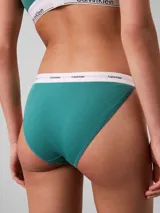 Conjunto de ropa interior de dos piezas compuesto por un corpiño triangular y una bombacha tipo tanga, ambos confeccionados en algodón con textura acanalada en color verde azulado. El corpiño cuenta con tirantes finos ajustables y una banda elástica inferior con el logo de la marca, mientras que la bombacha presenta un corte de talle medio con la misma banda elástica distintiva.