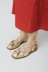 Sandalias bajas de cuero color marrón con tiras que se atan al tobillo.