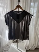 Remera plateada de efecto metalizado con un panel triangular de red negra en el pecho, cuello redondo y mangas cortas holgadas.