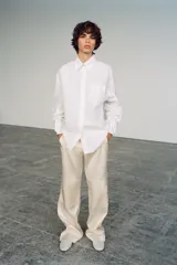Pantalón de tiro medio de tejido satinado color beige, con bolsillos laterales, pernera recta y detalle de tejido superpuesto en las rodillas. Cierre frontal con cremallera, botón interior y ganchos metálicos ocultos.
