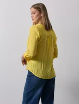 Blusa blanca de gasa marca Zac & Rachel, con cuello a la base, escote en V, abertura central con botones, bolsillo aplicado en el pecho y mangas largas regulables con presilla y botón. Tiene terminación opcional de nudo en el ruedo.