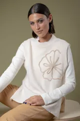 Chaleco de lana color crema con diseño de flor bordada en relieve en el frente, cuello redondo y aberturas laterales en el ruedo.