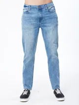 Pantalón jean de corte slim, color azul medio con efecto desgastado y sutiles roturas.