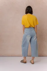 Pantalón de jean estilo barrel con tiro alto y pierna amplia de diseño curvo. Presenta un lavado celeste claro con efecto desgastado, cierre y botón frontal, y bolsillos funcionales.