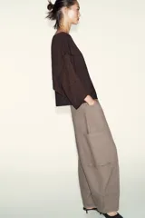 Jersey de punto marrón oscuro con hilo metalizado, cuello bote y manga ancha. Presenta un diseño asimétrico en la parte delantera con una capa superpuesta diagonal.