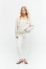Chaqueta bomber color beige melange, de lino, con cuello mao, cierre frontal con botones a presión, dos bolsillos con solapa en el pecho y puños y cintura elastizados.