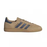 Championes adidas Handball Spezial de diseño clásico, confeccionados en gamuza color beige con las icónicas tres tiras laterales y refuerzo en el talón en color azul. Presentan suela de goma color caramelo y el nombre del modelo grabado en dorado en el lateral.