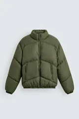 Cazadora acolchada tipo puffer de corte relajado, color verde militar. Presenta cuello subido, cierre frontal con cremallera, bolsillos laterales con cierre y puños elásticos.