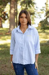 Camisa de lino color celeste, con cuello clásico, cierre frontal de botones y detalle de cuatro estrellas bordadas en color amarillo sobre el pecho. Presenta mangas tres cuartos con detalle de encaje en los puños.