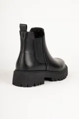 Bota estilo Chelsea de caña baja confeccionada en cuero sintético, con punta redonda, paneles elásticos laterales y suela track dentada de plataforma.