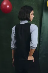 Mono largo de color negro con cierre frontal de botones vintage de distintos colores. Presenta un diseño sin mangas, con bolsillos laterales y una cinta para herramientas en la parte trasera.