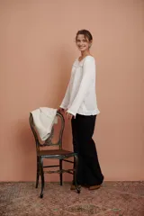 Blusa blanca de manga larga con puntilla de flores en el escote y volado en el ruedo.