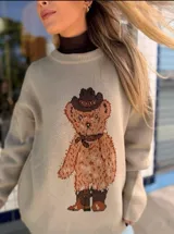 Sweater de punto color marrón claro, con diseño de oso estampado en el frente. Presenta cuello redondo, mangas largas con puños ajustados y corte holgado.