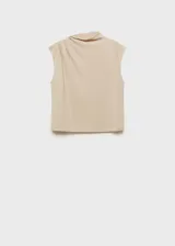 Camiseta color beige con cuello alto asimétrico, sin mangas y detalles fruncidos. Tejido fluido y diseño recto.